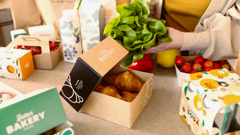 Groceries in cartonboard packaging at a table.