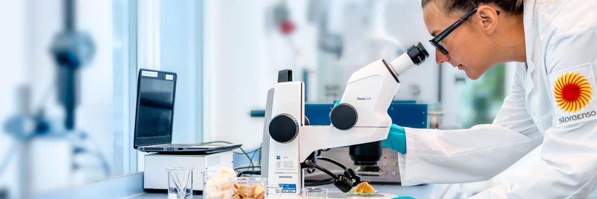 Laboratory employee looking at a sample in a microscope .