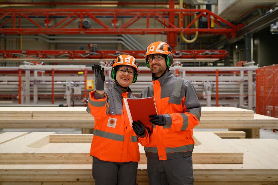 Employees in safety gear, standing in front of sawn wood.